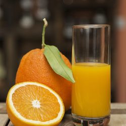 closeup shot of a glass of orange juice and fresh oranges on a wooden crate with blurry background